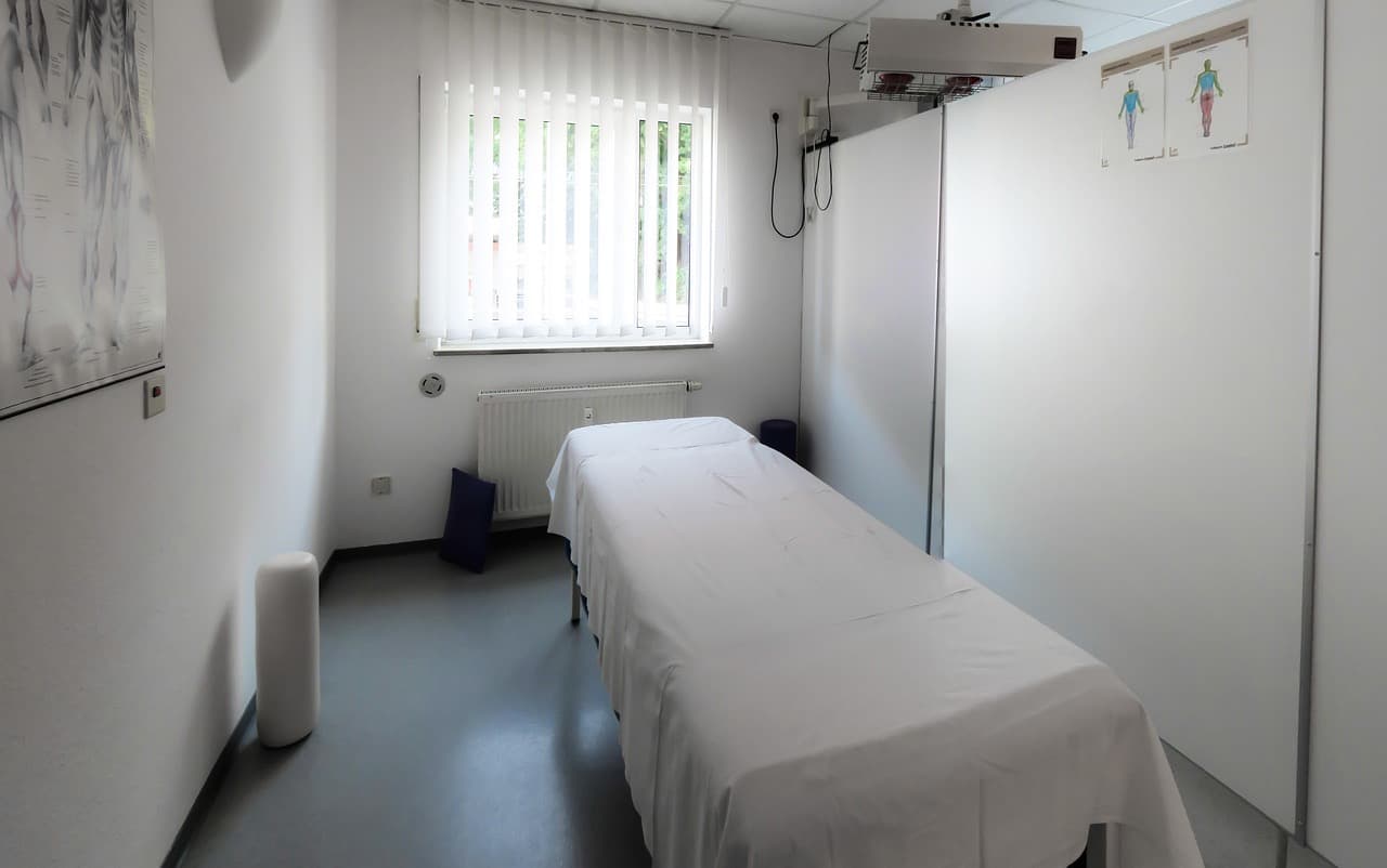 Tedavi masası, anatomi posteri ve kızılötesi lambası olan sade bir fizyoterapi tedavi odası